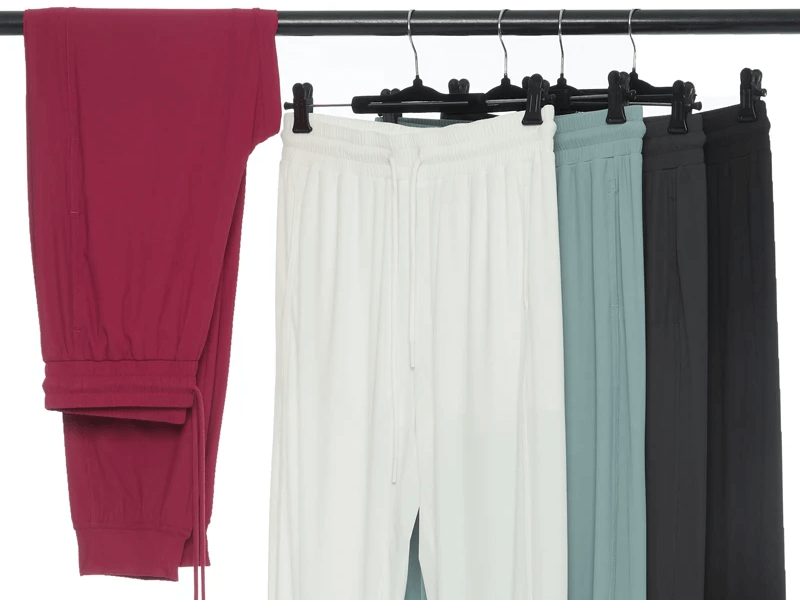 Women's joggers in red, white, blue, and black hanging on a rack, showcasing stylish versatility in activewear fashion.
